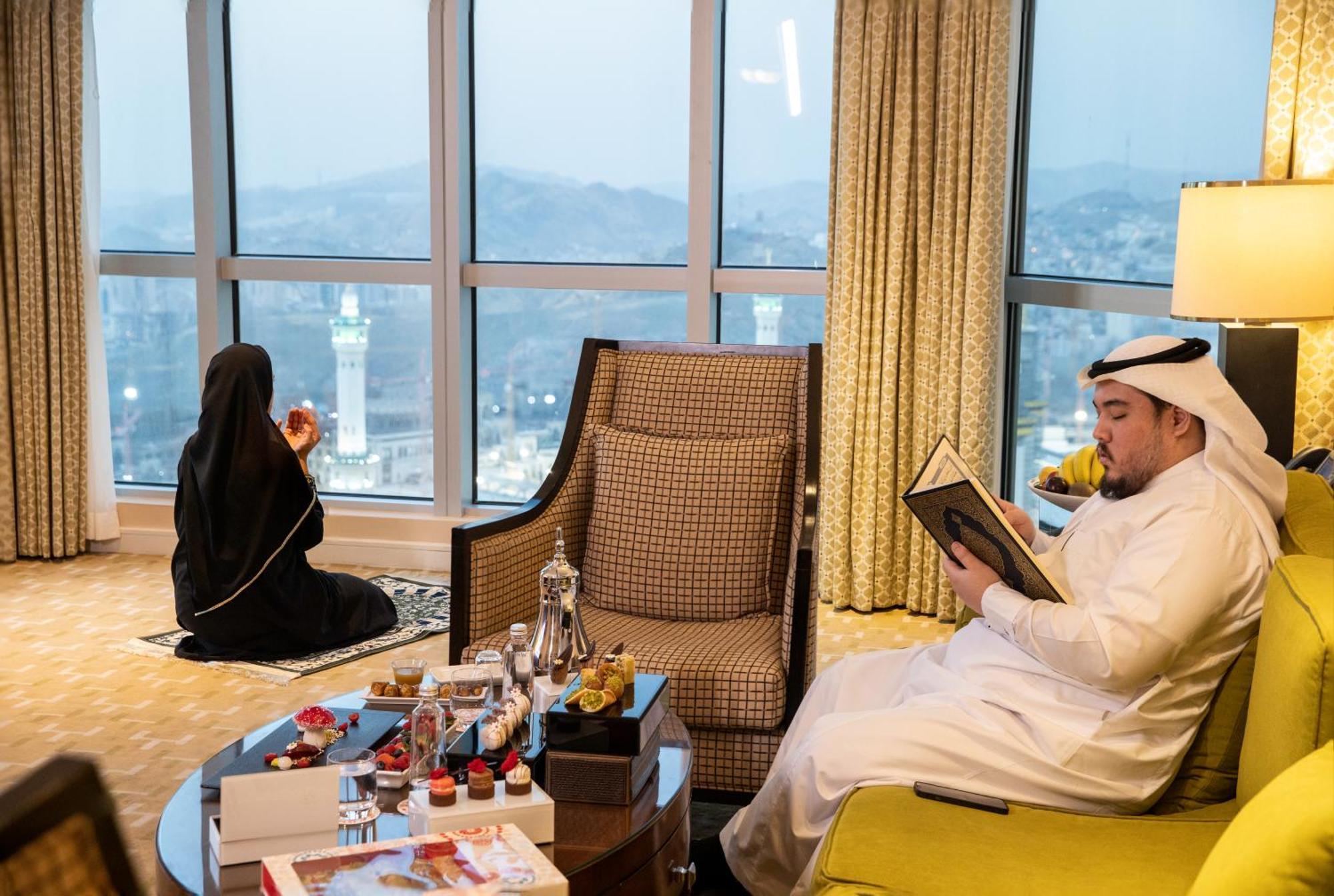 Swissotel Al Maqam Makkah Meca Exterior foto The photo depicts a scene inside a hotel room or a suite with large windows providing a view of a cityscape, likely near a landmark. 

In the foreground, there is a stylish coffee table adorned with several decorative items, possibly including small 