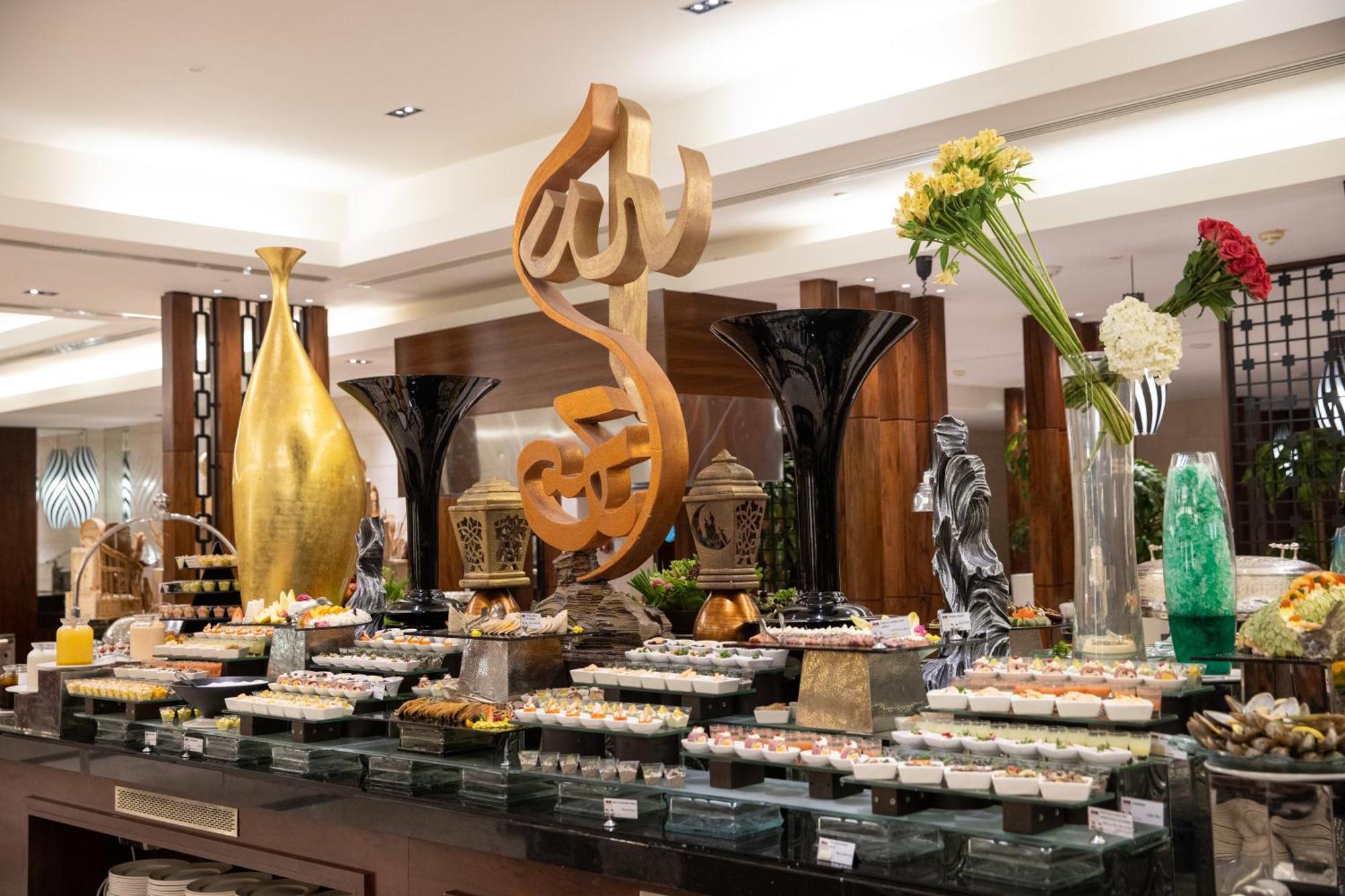 Swissotel Al Maqam Makkah Meca Exterior foto The photo displays a beautifully arranged buffet set up in a restaurant or hotel. In the center, there is an artistic sculpture featuring a stylized calligraphic design. Surrounding it are various decorative elements, including vases and floral arran