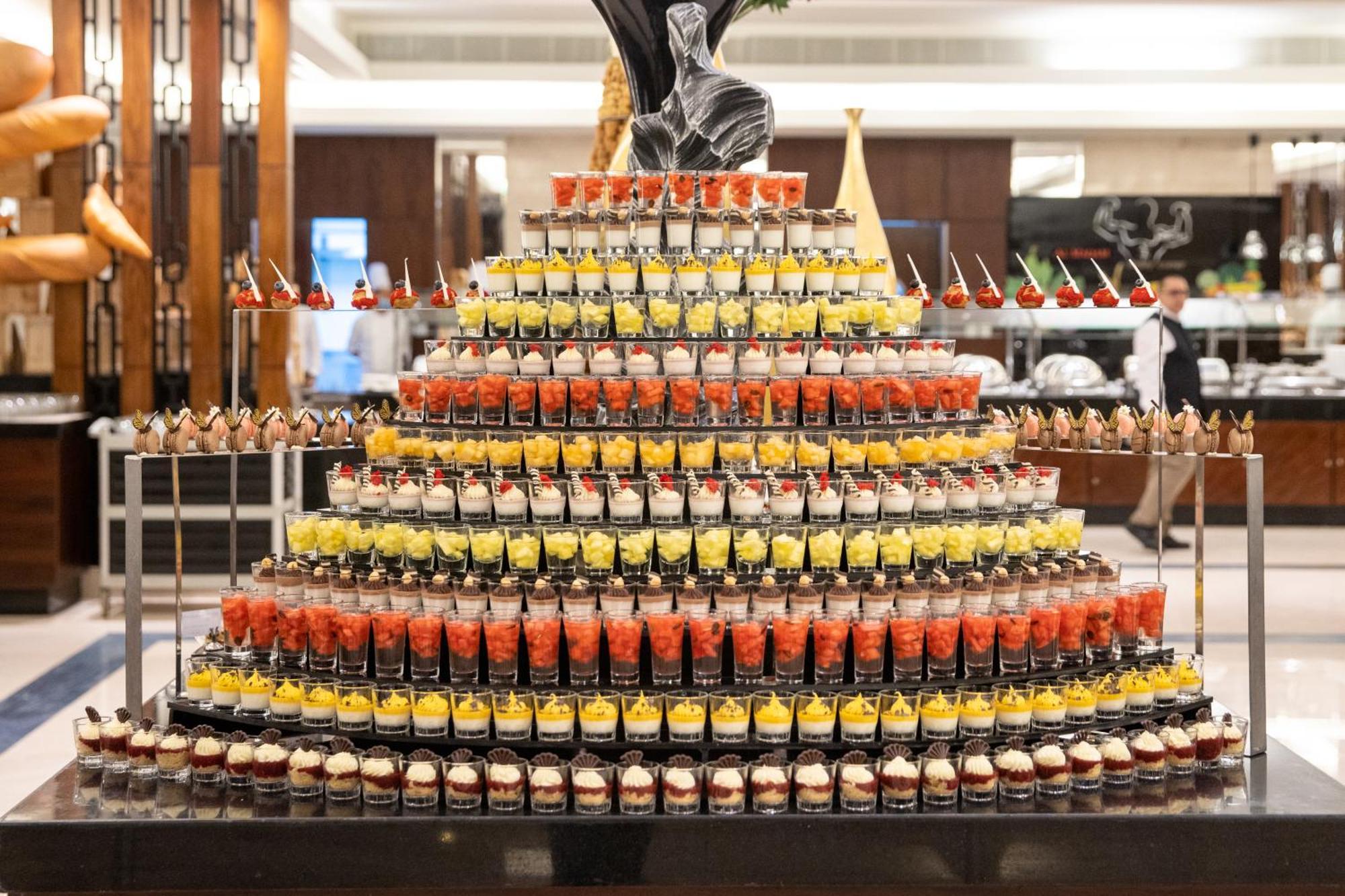 Swissotel Al Maqam Makkah Meca Exterior foto The photo shows an elaborate display of desserts arranged in a tiered, pyramid-like structure. The arrangement consists of numerous small cups filled with various colorful desserts, including layers of fruity and creamy elements. The cups are stacked